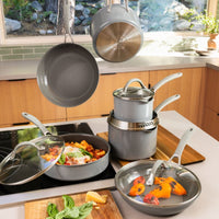 Gray Circulon cookware set in a sunny kitchen: pasta in a sauté pan on an induction cooktop, stacked saucepans, hanging pans and peppers in a lidded frying pan