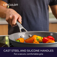 Cast steel and silicone handles for a secure, comfortable grip: hand holding a gray frying pan of mini sweet peppers on a cooktop
