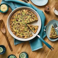 Top view of a marine blue frying pan holding a mushroom frittata with one slice cut out and served on a plate beside it