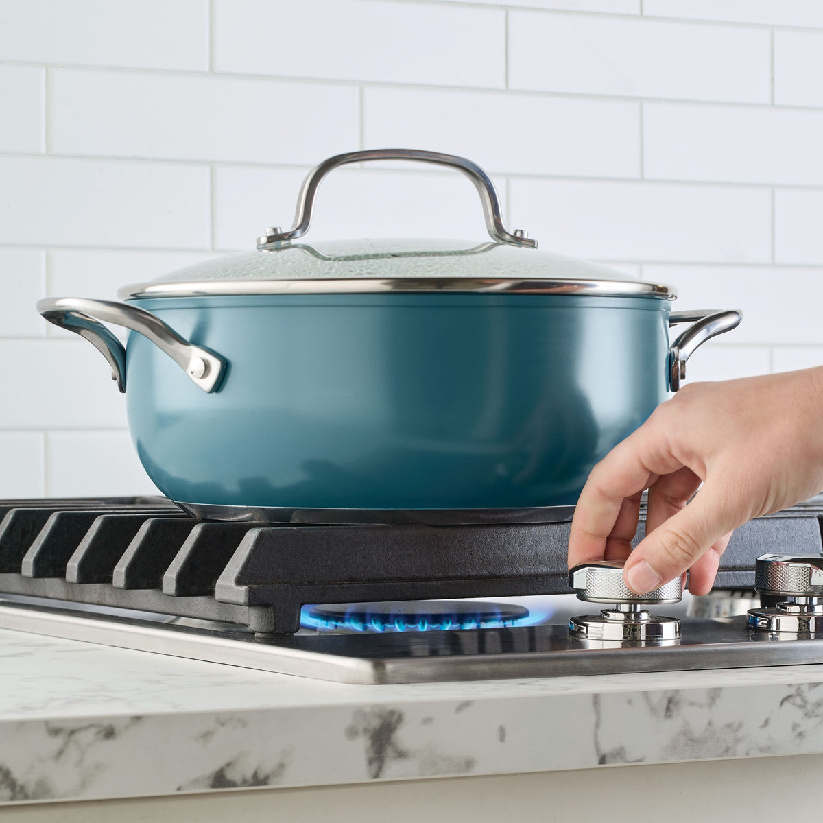 Agave blue 4-quart casserole with glass lid on a gas stove as a hand turns the burner knob