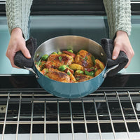 Hands with dark towels lifting an agave blue casserole of roasted chicken, potatoes and Brussels sprouts out of an oven