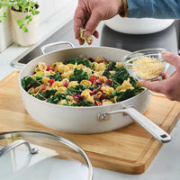 Porcelain white sauté pan of orecchiette with spinach and tomatoes on a wooden board, cheese sprinkled on top