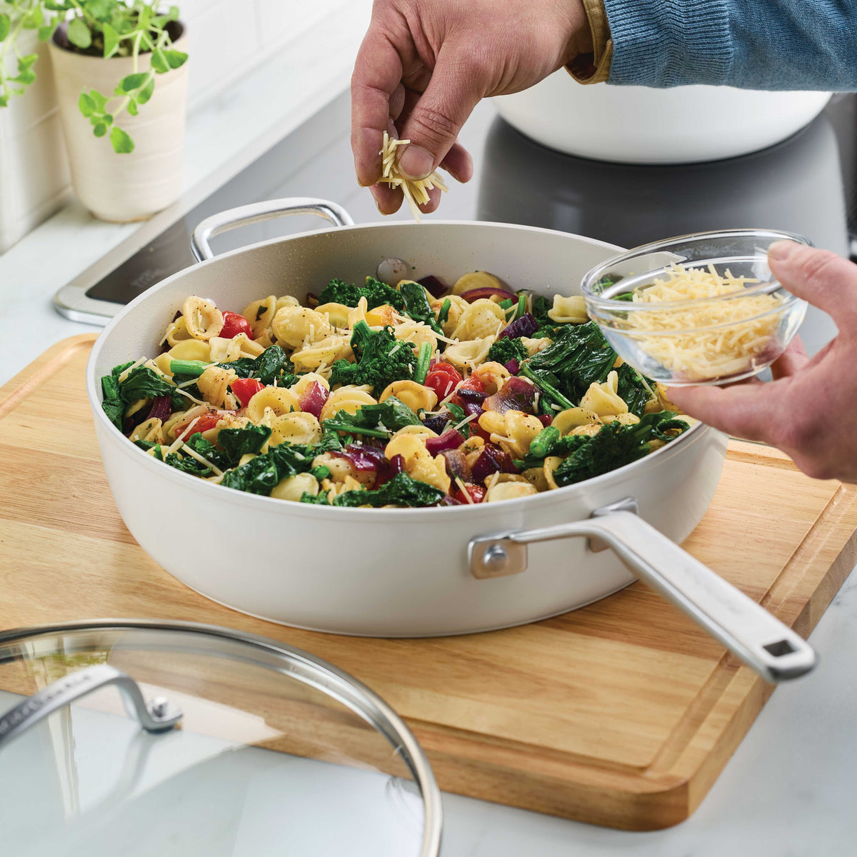 Porcelain white sauté pan of orecchiette with spinach and tomatoes on a wooden board, cheese sprinkled on top