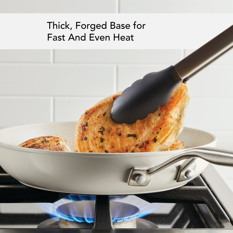 Thick, forged base for fast and even heat: tongs turning chicken breasts in the porcelain white ceramic frying pan over a gas flame