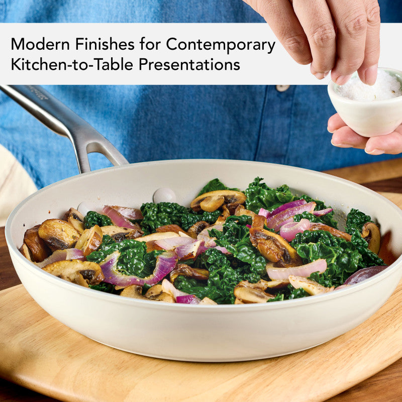 Modern finishes for contemporary kitchen-to-table presentations: porcelain white frying pan of sautéed kale, mushrooms and red onion, with a hand adding salt