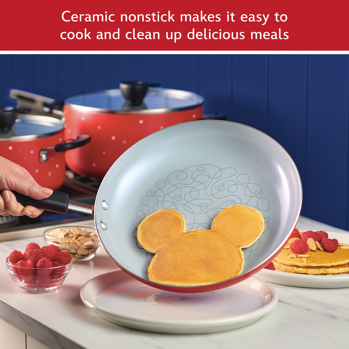 Ceramic nonstick makes it easy to cook and clean up delicious meals: red frying pan sliding a Mickey Mouse shaped pancake onto a plate, red pots behind