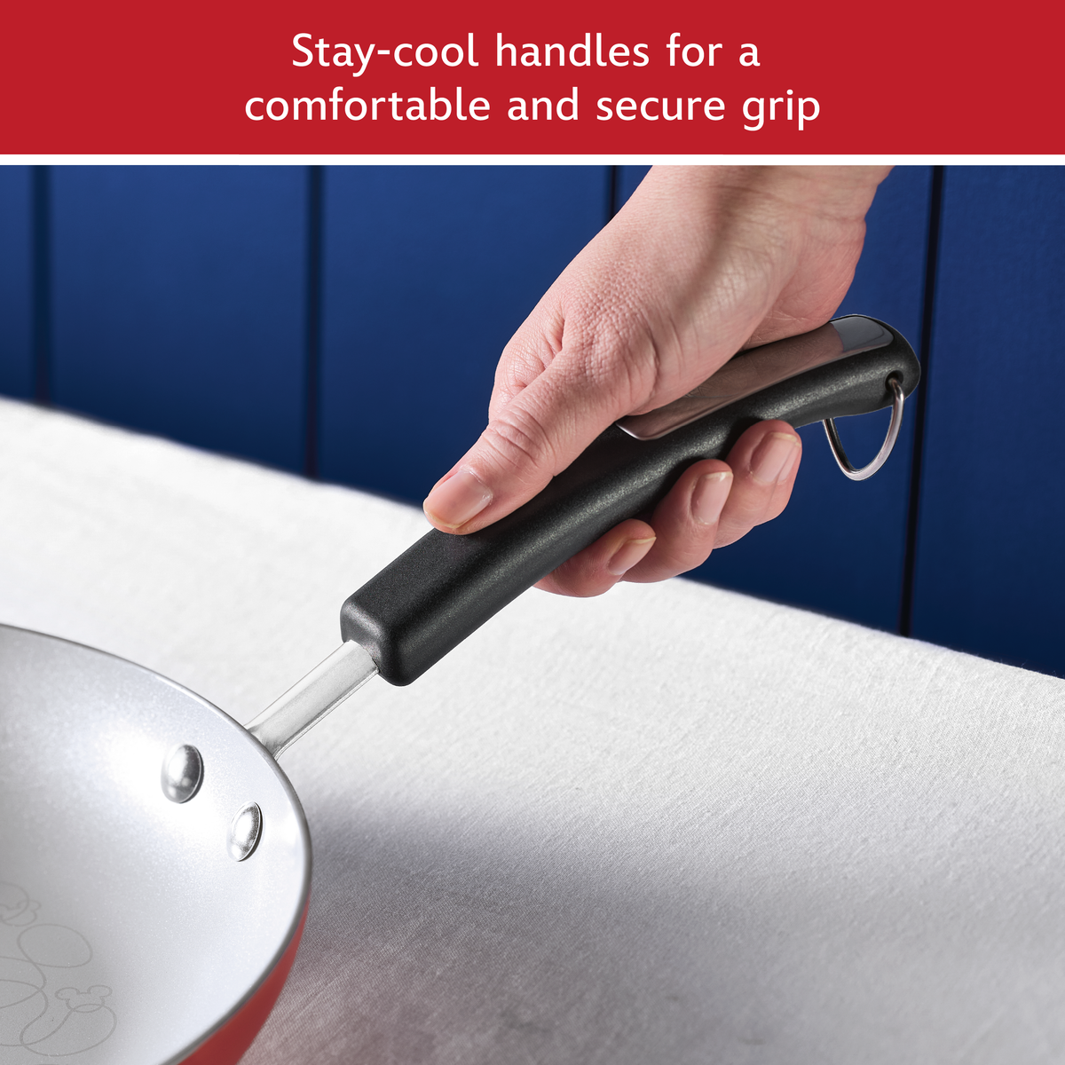 Stay-cool handles for a comfortable and secure grip: hand holding the black handle of a red ceramic nonstick frying pan