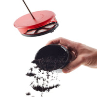 Hand tipping used coffee grounds out of the black filter cup below the red plunger lid