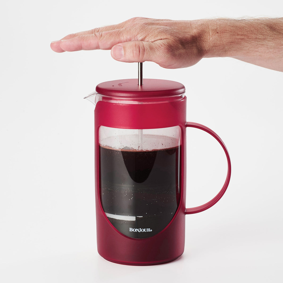 Hand pressing down the plunger of the red French press full of coffee