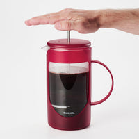 Hand pressing down the plunger of the red French press full of coffee
