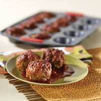 Mini meatloaves baked in the red-handled muffin pan, with three on a green plate in sauce